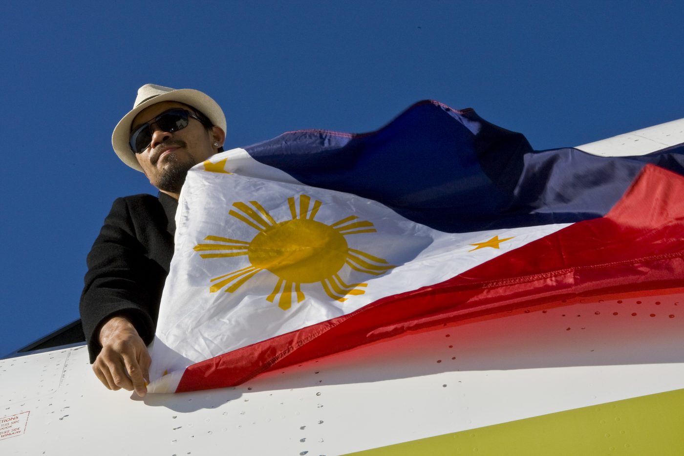 Manny Pacquiao holding the Philippine flag against a clear blue sky.